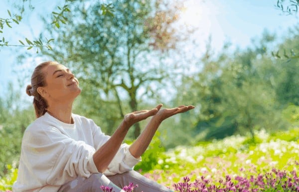 A woman sitting in a field of flowers feeling peaceful, representing the clear energy after cleansing rose quartz.