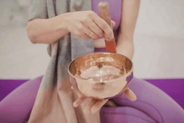 A person using a mallet on a singing bowl to clear crystal vibrations.