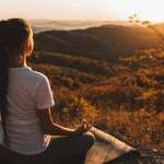 Woman meditating alone on hill with amazing autumn mountain view