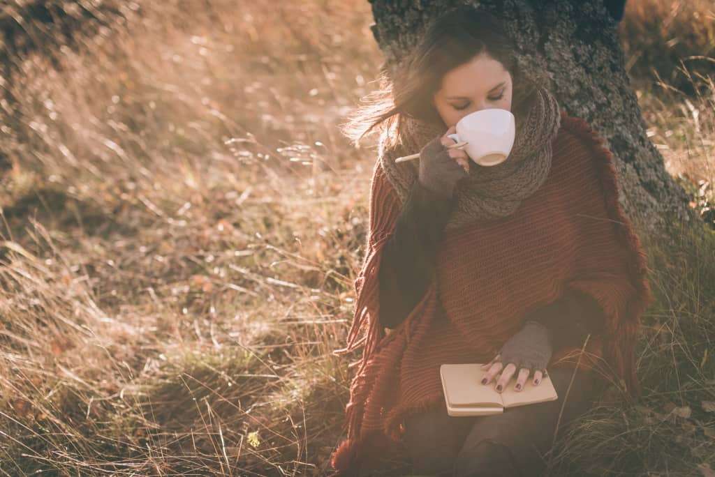 person drinking tea under tree, writing in their journal