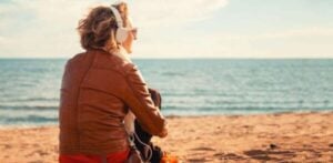 Person sitting on beach with headphones listening to instructions about how to use hypnosis for clearing negativity from your life