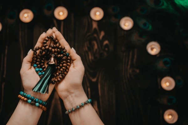hands holding mala beads around candles used as a spiritual meditation gift