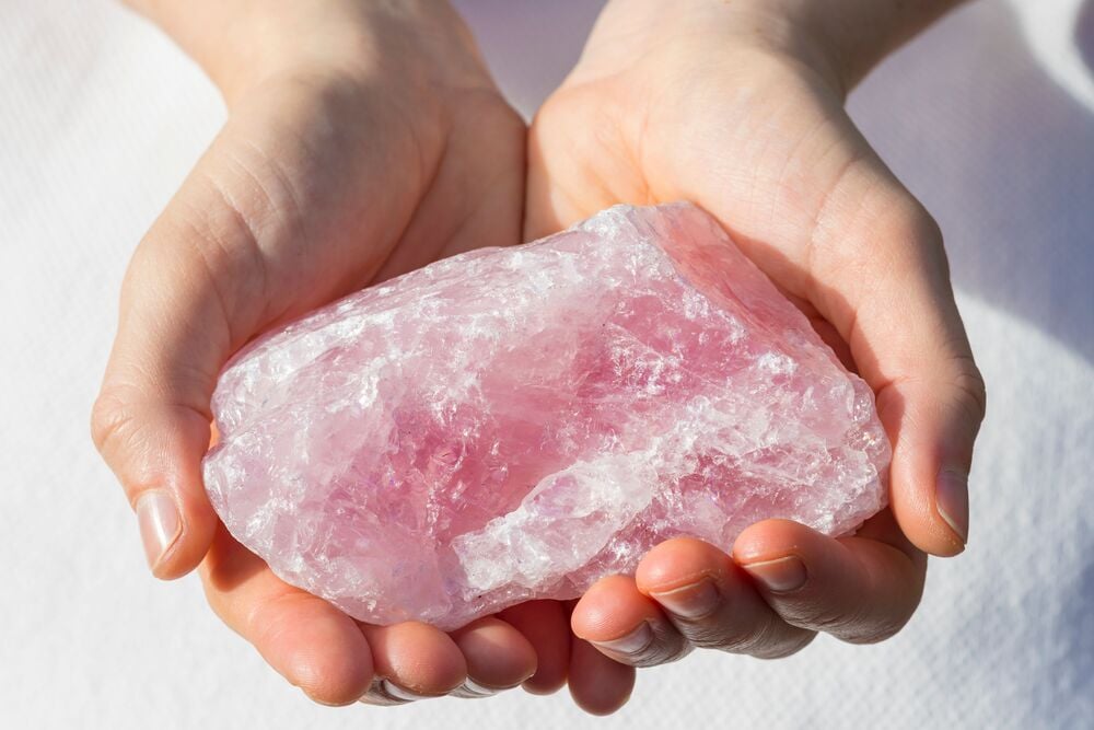 hands holding raw rose quartz stone