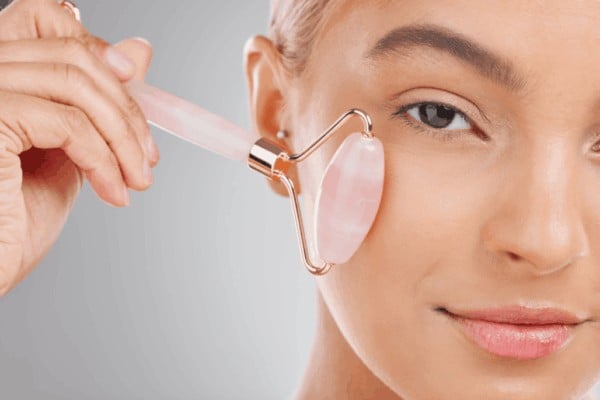 Person using a rose quartz facial roller to gently massage the under-eye and cheek area for a cooling effect.