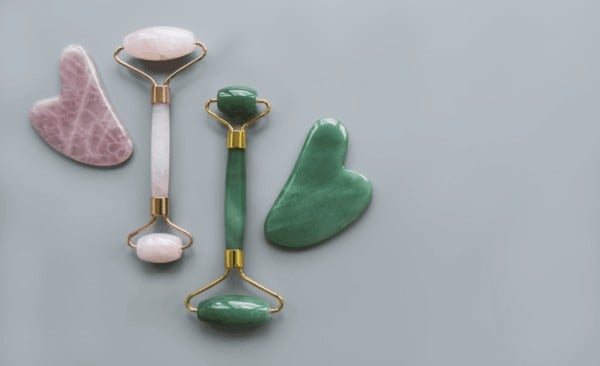 Comparison of a pink rose quartz facial roller and gua sha tool next to a green jade roller set.