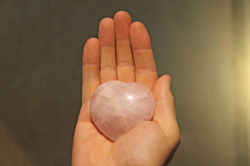 a pair of hands holding various pieces of rose quartz jewelry