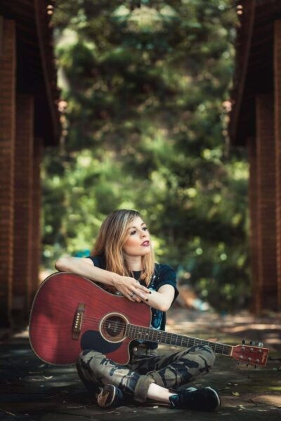 person outdoors near tree with guitar letting their voice chakra be heard