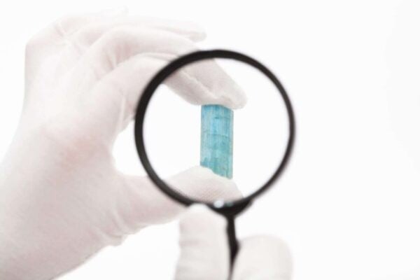 Hand looking at Aquamarine stone under magnifying glass