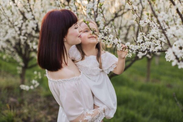 mother holding child and breathing in fragrances near flowering tree