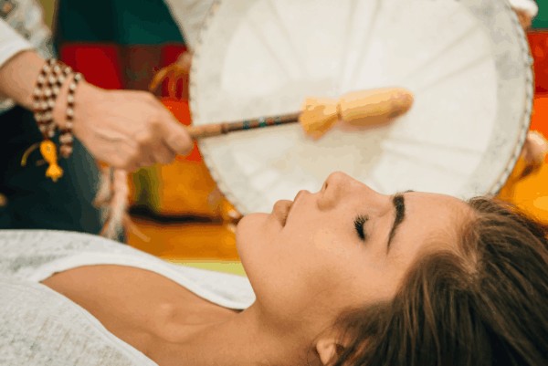 person receiving a sound bath experience whilst other person is drumming