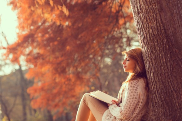 person outdoors sitting against a tree setting intentions with journal
