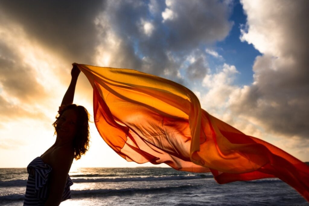 person floating orange fabric in air as they walk in water to connect with sacral energy
