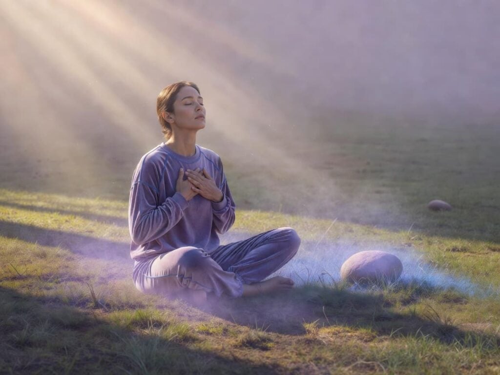 person outdoors in nature and sunlight, hands on chest for breath awareness in mindful session
